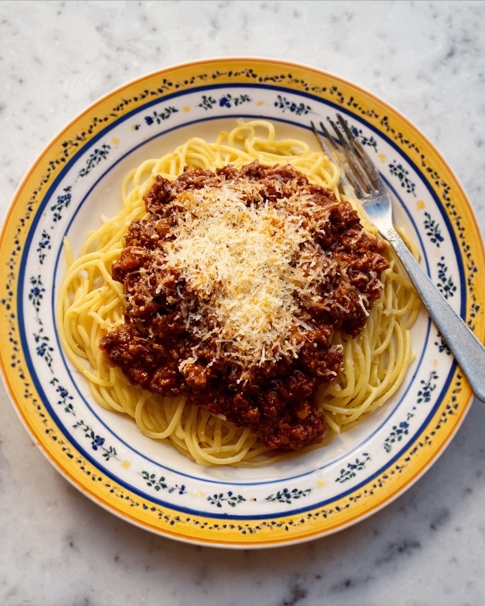 The dish is a round plate of white color with a blue and yellow decorative edge, placed on a white marbled surface. It has a base layer of light yellow spaghetti noodles, coiled loosely across the plate. On top of the noodles, there is a thick, rich layer of brown meat sauce with visible small bits of meat. The sauce covers most of the noodles but leaves the edges exposed. Sprinkled generously on the top layer is a fine, grated white cheese, slightly melting into the warm sauce. A silver fork is placed to the right side of the plate. The photo is taken with an iphone --ar 4:5 --v 7