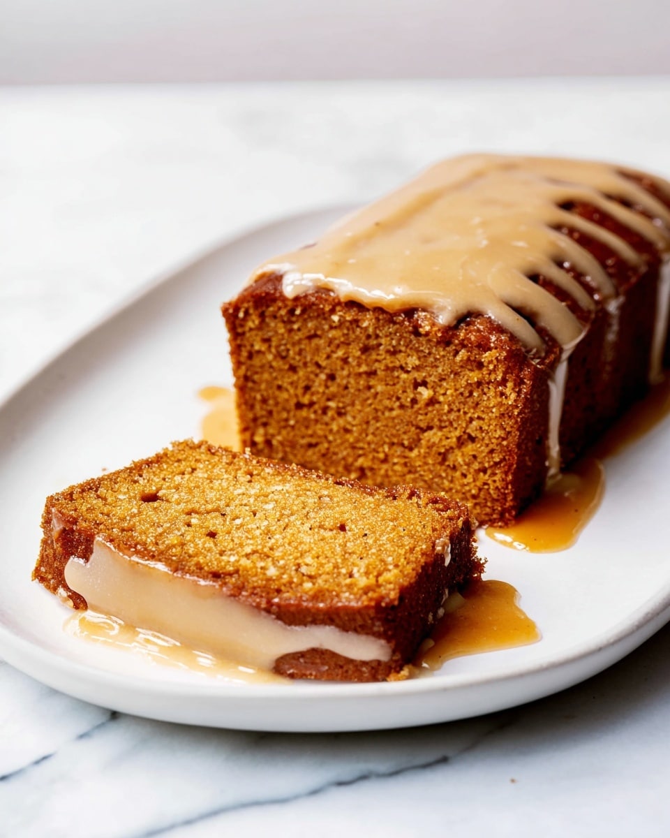 The image shows a rectangular cake with one slice separated from the main piece, placed on a white plate. The cake has a warm brown color and a moist texture. There is a light beige sauce poured over the top and sides of the cake, pooling slightly on the white plate. The cake appears soft with a slightly coarse crumb, and the sauce has a smooth, glossy finish. The background is a white marbled texture. photo taken with an iphone --ar 4:5 --v 7