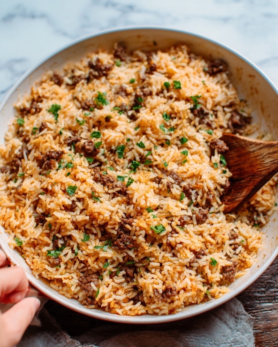 A close-up of a large white bowl filled with cooked rice mixed with small pieces of browned meat, evenly spread throughout. The rice has an orange tint and looks fluffy, with small green herbs sprinkled on top for a fresh touch. A woman's hand is seen holding a wooden spoon inside the bowl, stirring the food. The bowl is placed on a white marbled surface, and the overall image has warm, natural lighting. photo taken with an iphone --ar 4:5 --v 7