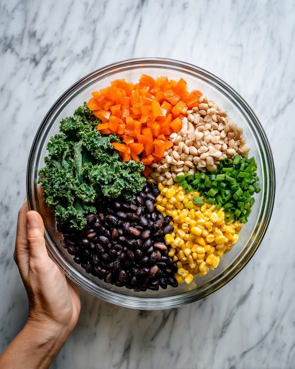 A clear glass bowl divided into five sections filled with different colorful ingredients placed on a white marbled surface. The top section holds small diced orange bell peppers. Below it to the right is a pile of chopped light beige nuts or grains. Next to that are small chopped green onions. Below the green onions is a bright yellow corn layer. To the left, black beans fill a section with dark, shiny texture. A piece of green kale is placed on the left side, overlapping parts of the black beans. A woman's hand is seen holding the bowl at the bottom edge. Photo taken with an iphone --ar 4:5 --v 7