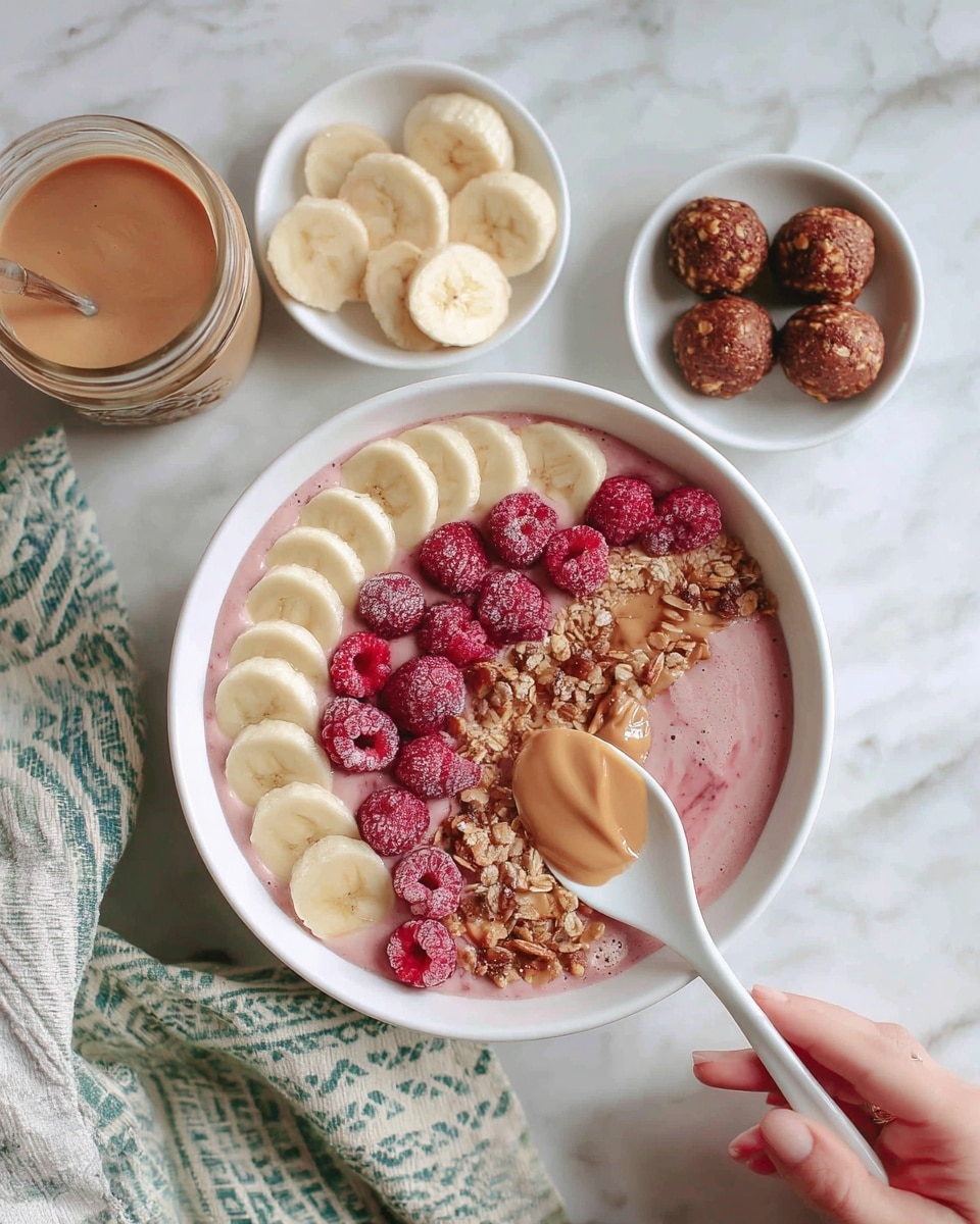 The image shows a white bowl filled with several distinct layers on a white marbled surface. At the bottom of the bowl is a creamy pink smoothie base, topped neatly with thin slices of banana arranged in a semi-circle on one side. Next to the bananas, there is a cluster of bright pink raspberries and a spoonful of light brown nut butter. A small pile of granola sits in the center, adding a crunchy texture. Around the bowl, there are small white dishes holding slices of banana, more raspberries, and round brown energy balls. A jar with a light brown sauce is placed nearby, and a woman’s hand is seen holding a white spoon ready to scoop from the bowl. A patterned cloth with green and blue lines is also visible in the corner. Photo taken with an iphone --ar 4:5 --v 7