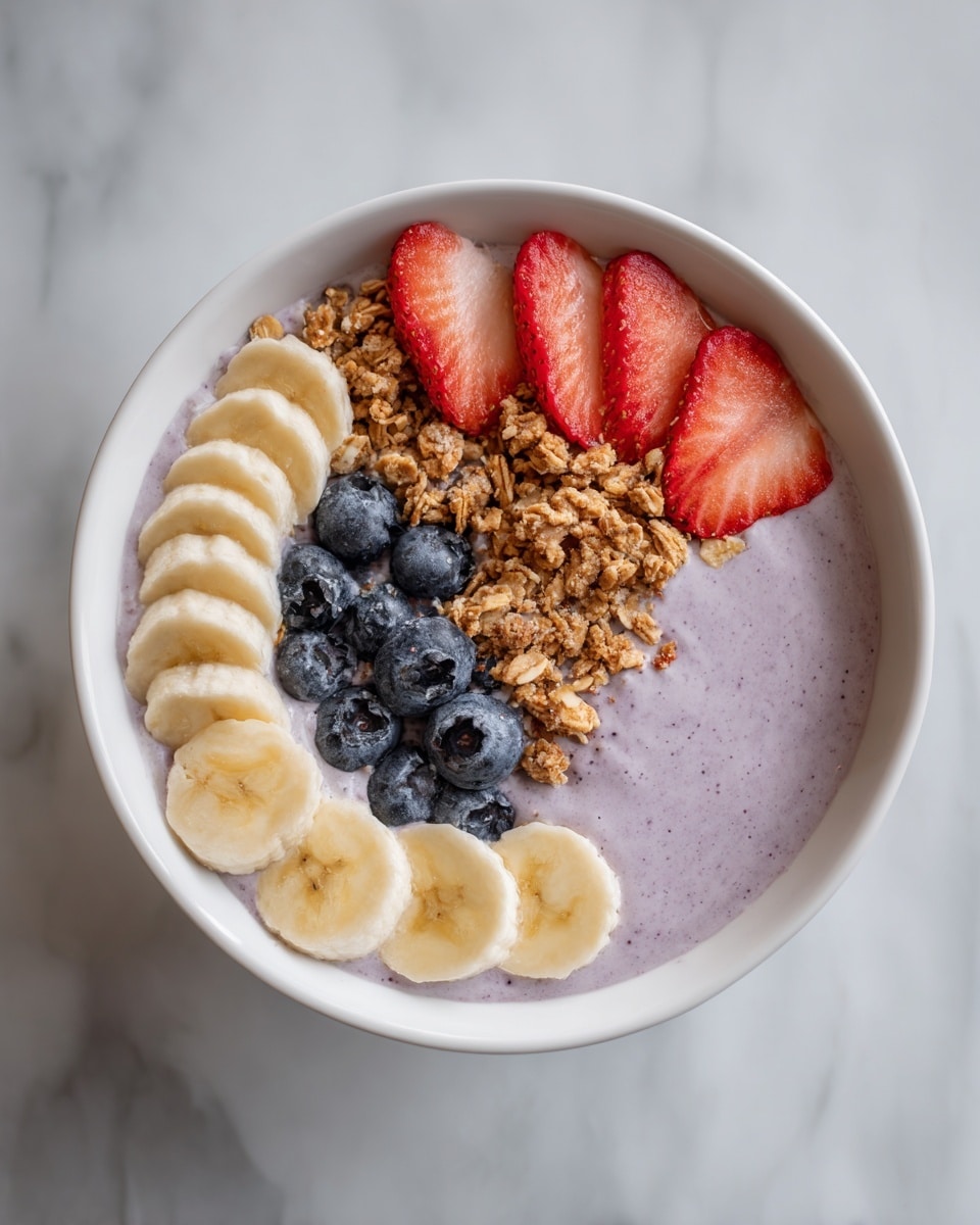 A white bowl filled with a thick, smooth light purple smoothie base in the center. On top, there are four red strawberry slices arranged in a fan shape near the top right, a pile of light brown granola just below the strawberries, a cluster of dark blue blueberries arranged near the top left, and a neat row of light yellow banana slices lining the bottom edge of the bowl. The bowl sits on a white marbled surface. Photo taken with an iphone --ar 4:5 --v 7