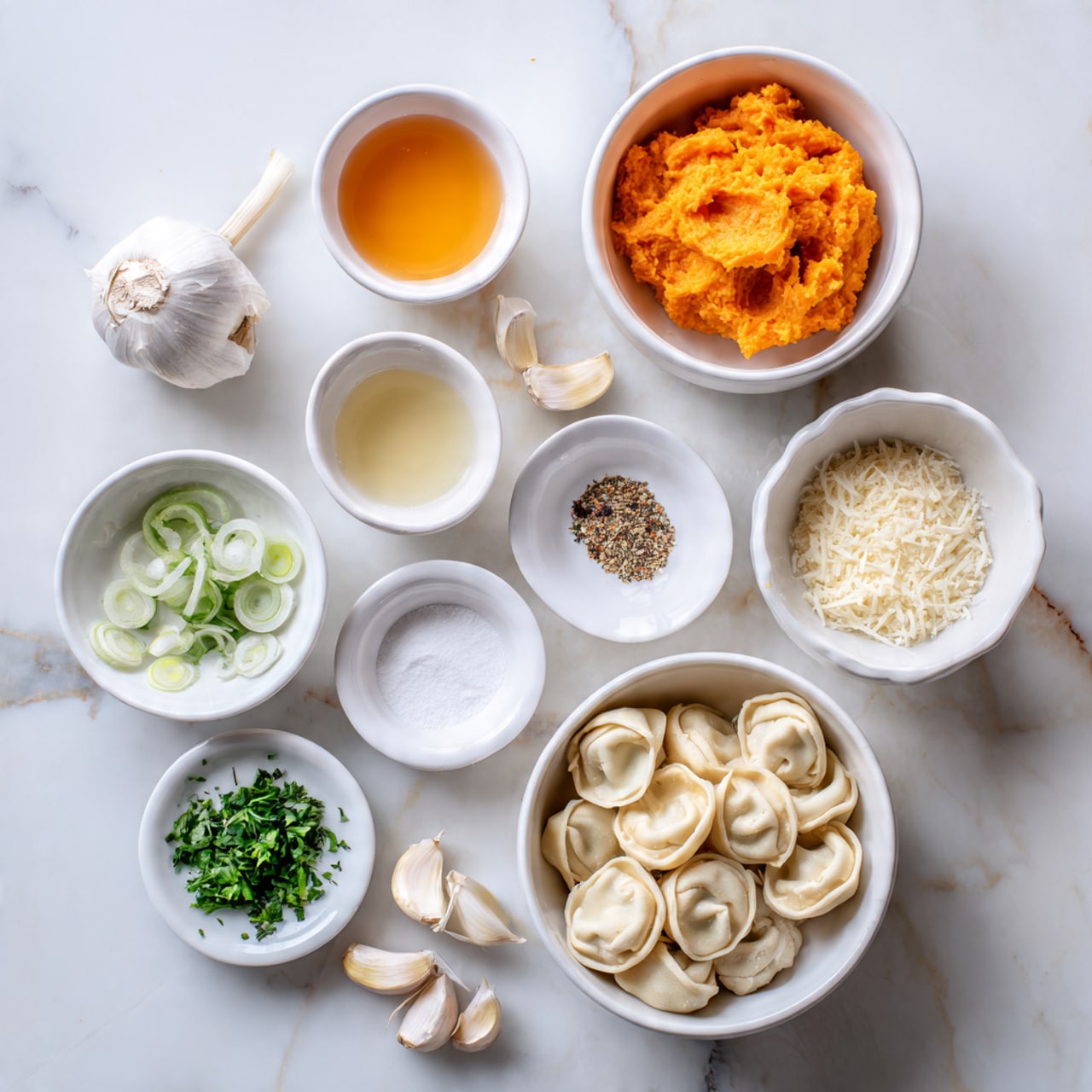 The image shows several small white bowls and plates arranged on a white marbled surface. There is a white bowl filled with orange mashed mixture, likely a sauce, and nearby are four other white bowls containing clear liquid, light amber liquid, white powder, and a white creamy liquid. On one white plate, there are chopped green herbs and slices of shallots. Another white plate holds cloves of garlic, some light brown spices, and white salt. A white bowl contains grated cheese, and a larger white bowl is filled with round stuffed pasta, possibly tortellini. The setup looks clean and organized, ready for cooking. Photo taken with an iphone --ar 4:5 --v 7