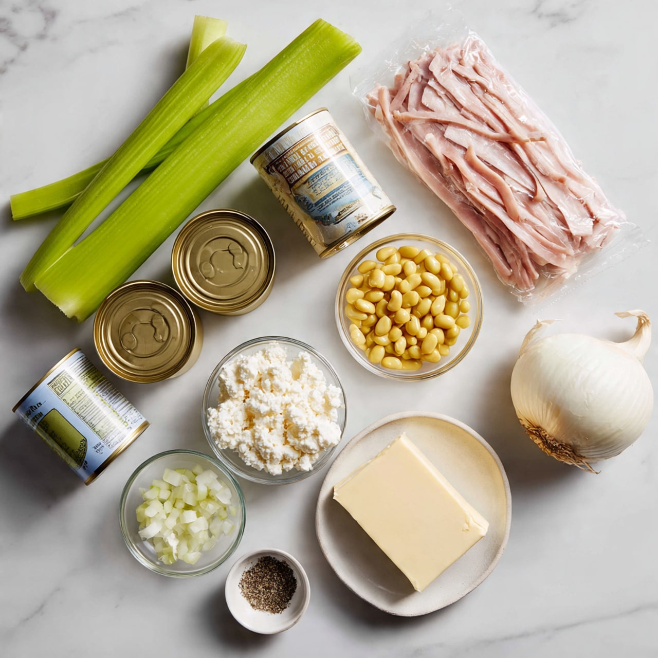 The image shows several cooking ingredients arranged on a white marbled surface. There are three green celery stalks placed diagonally on the left side. Nearby, there are three cans of beans and a can of cream of mushroom. To the right, there is a package of smoked ham strips wrapped in plastic. In front of these ingredients, there is a small pile of yellow bouillon cubes, a small glass bowl with chopped white onions, a small glass bowl with minced garlic, a cup filled with cottage cheese, a block of butter, and a small white bowl with black pepper. The arrangement is clean and evenly spaced, all items clearly visible. photo taken with an iphone --ar 4:5 --v 7