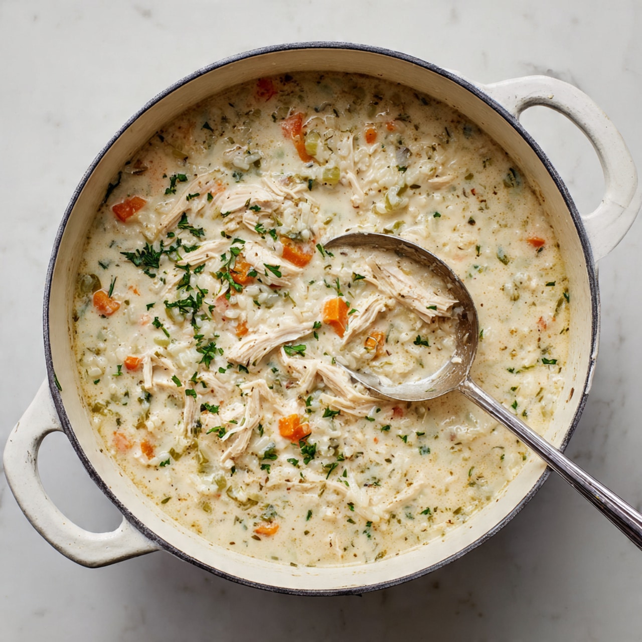 A large white pot filled with creamy chicken and rice soup sits on a white marbled surface. The soup has a thick, creamy texture with visible pieces of shredded light-colored chicken and small orange carrot chunks. Fresh green herbs are sprinkled throughout, adding small bright green dots on the surface. A silver ladle is partially buried in the soup, scooping some of the mixture. The pot has a simple design with two handles, and the scene is bright and clear. Photo taken with an iphone --ar 4:5 --v 7