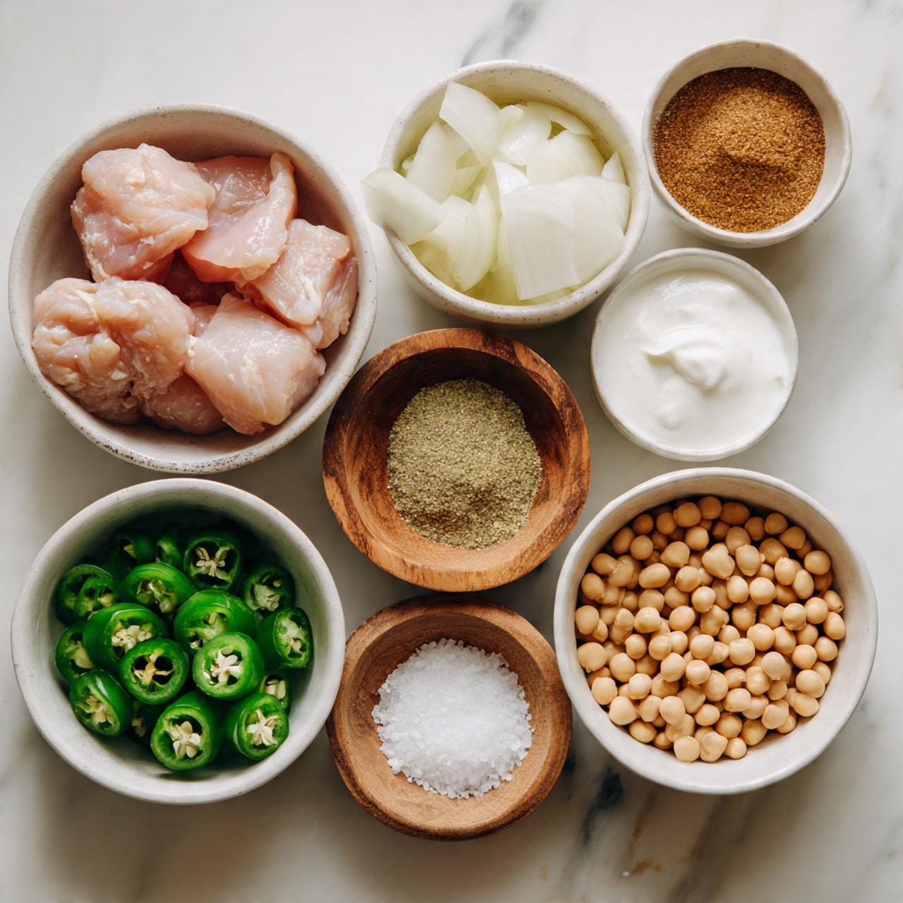 A collection of six white bowls arranged closely on a white marbled surface, each holding different ingredients: one bowl in the center with light pink chunks of raw chicken, a bowl above it filled with pale sliced onions, another bowl above and to the right containing a coarse brown spice powder, a white bowl next to the spice holding thick white yogurt, a bowl below with bright green sliced jalapeños, and another bowl below the onions with light brown soybeans. In the middle between the onion and chicken bowls is a small wooden bowl with coarse white salt. The colors range from pale off-white to light pink, dark green, brown, and beige, creating a fresh and simple look. photo taken with an iphone --ar 4:5 --v 7