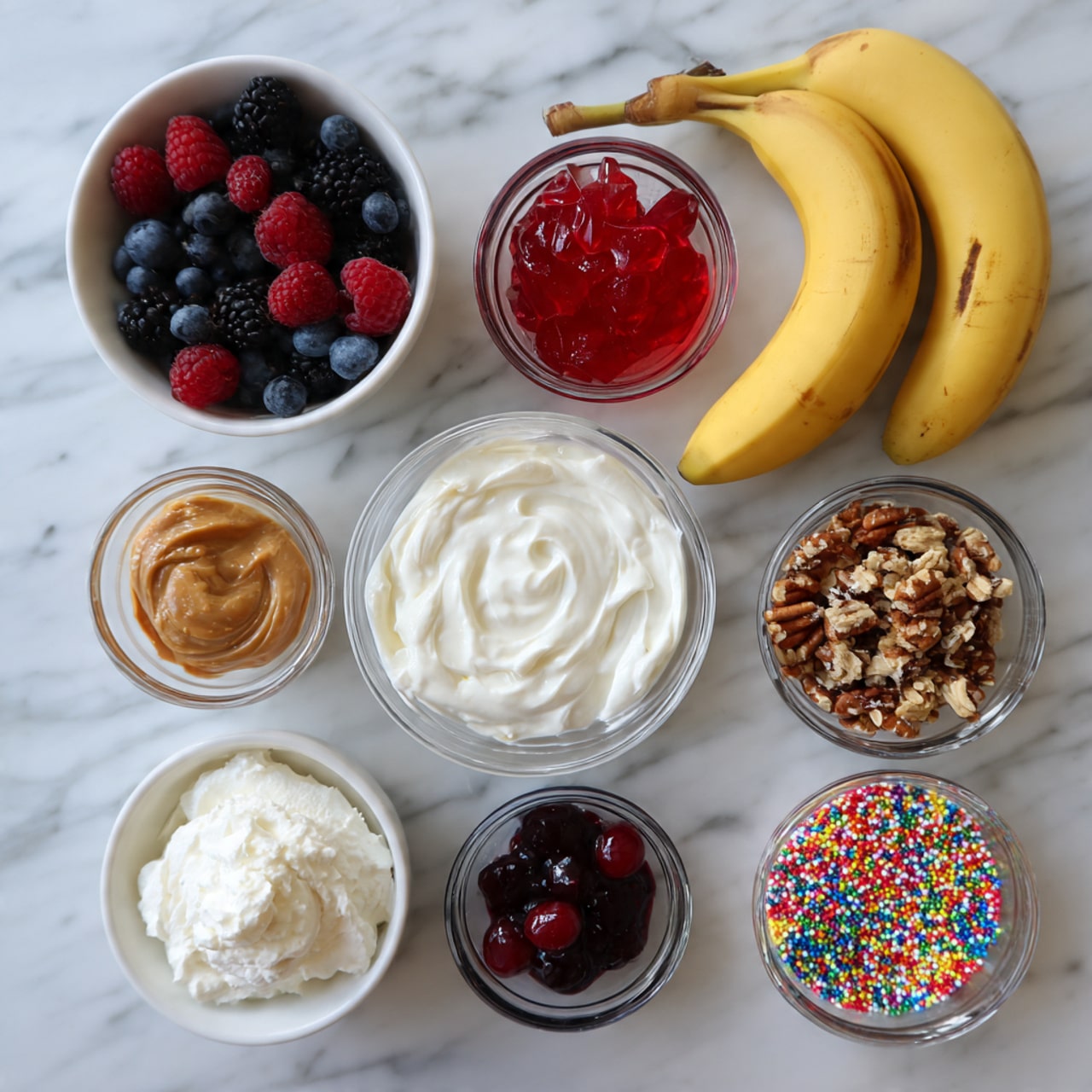 A top-down view of nine small bowls and two bananas arranged on a white marbled surface. In the top left is a white bowl filled with mixed berries including blueberries, blackberries, and raspberries. To its right, two ripe yellow bananas with brown spots rest. Below the berry bowl is a small clear bowl with red jelly, and next to it is a white bowl filled with thick white yogurt. Beneath the jelly bowl is a small clear bowl containing peanut butter. In the center is a clear bowl with dark purple berry jam. To the right are two white bowls, one with chopped pecans and the other with granola clusters. Below these are two more clear bowls, one with white whipped cream and one with colorful rainbow sprinkles. Lastly, at the bottom left is a small clear bowl with two bright red maraschino cherries. Photo taken with an iphone --ar 4:5 --v 7
