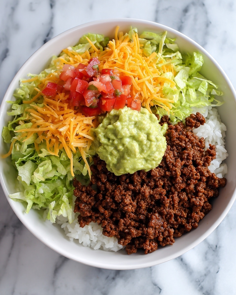 This image shows a bowl of food with five clear layers. At the bottom, there is a soft bed of white rice. On top of the rice, there is a thick layer of dark brown cooked ground meat with a crumbly texture. Over the meat, scattered fresh green lettuce pieces add a crisp look. Bright orange shredded cheddar cheese is sprinkled next, adding a slight shine. At the top, there is a dollop of creamy, light green guacamole alongside small, red diced tomatoes. The bowl is white and sits on a white marbled surface. Photo taken with an iphone --ar 4:5 --v 7