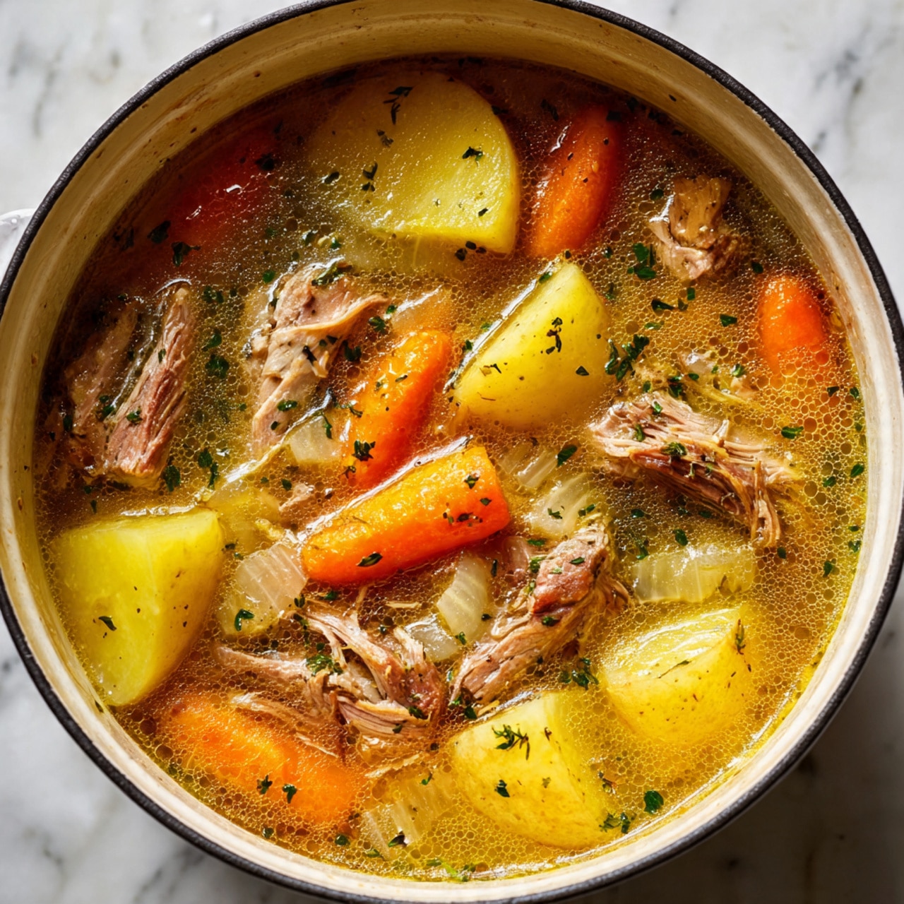 The image shows a close-up of a pot filled with a warm stew. It has large pieces of light brown cooked meat spread throughout the dish. The broth is a golden yellow color with small bubbles on the surface. There are several bright orange carrot slices and chunks of yellow potato mixed in. Thin slices of translucent onion are visible floating in the broth. Small bits of green herbs are sprinkled across the top, adding color contrast. The stew looks rich and hearty, with a mix of soft vegetables and tender meat in a clear, flavorful broth. The pot is white inside, and the background has a white marbled texture. photo taken with an iphone --ar 4:5 --v 7