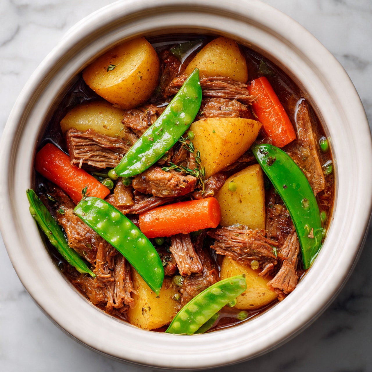 The image shows a close-up of a white cooking pot filled with a layered stew. The base layer is golden-brown thin meat slices spread evenly. On top are large, soft, golden potato chunks and bright orange carrot pieces scattered throughout. There are also bright green snap peas placed on top, adding a fresh pop of color. The background features a white marbled surface. Photo taken with an iphone --ar 4:5 --v 7