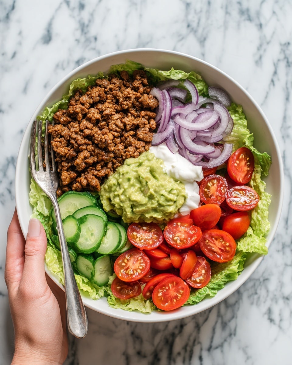 The image shows a white bowl filled with a colorful layered dish placed on a white marbled surface. The bottom layer is green lettuce leaves spread evenly inside the bowl. On top of the lettuce, there are sections of cooked brown ground meat, seasoned light brown cooked chicken pieces in the lower right, and halved bright red cherry tomatoes on the right. Thin slices of purple onion sit above the chicken, while green pickle slices are near the center. Dollops of creamy white sour cream and light green guacamole are also placed in the middle of the bowl. A fork rests on the left side of the bowl, and a woman's hand is visible holding the bowl from the left side. Photo taken with an iphone --ar 4:5 --v 7