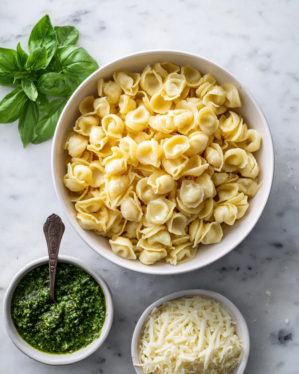 The image shows a round white bowl filled with many small, folded, golden-yellow pasta pieces on a white marbled surface. Below the bowl, there is a small white bowl with green pesto sauce and a spoon inside it. Next to the pesto, fresh green basil leaves lie on the surface. Below the basil, there is another small white bowl with finely shredded white cheese. The textures vary from smooth sauce to soft pasta and leafy herbs. The overall look is clean and fresh, with light and natural colors. photo taken with an iphone --ar 4:5 --v 7