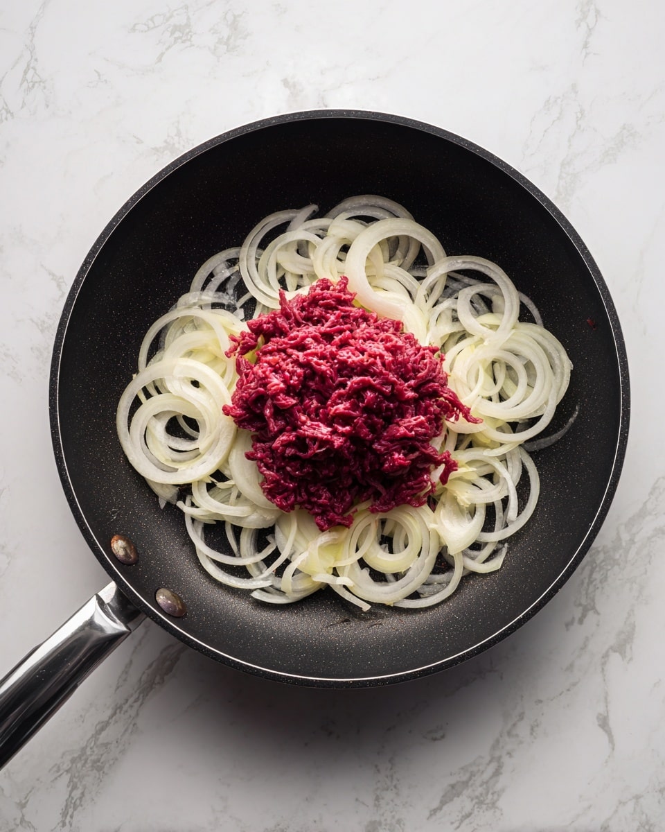 The image shows a close-up of a black frying pan on a white marbled surface. Inside the pan, there are two main layers: a base layer of light yellow, thin, and slightly translucent sliced onions arranged in a ring around the edge, and a center pile of raw, finely shredded red meat with a slightly moist texture. The onions surround the meat, creating a clear contrast between the pale rings and the deep red center. Photo taken with an iphone --ar 4:5 --v 7