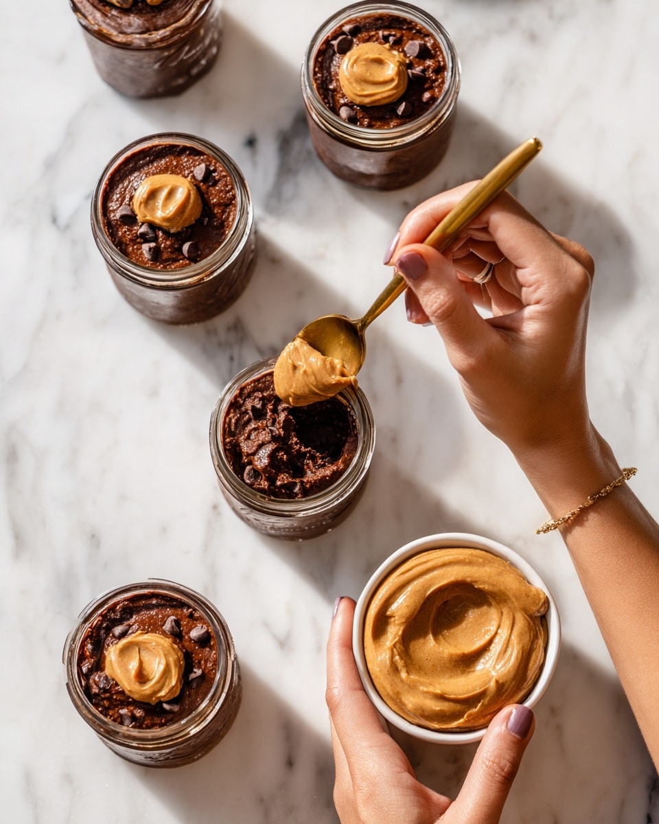 The image shows four small glass jars filled with a dark brown, thick chocolate mixture with visible small chunks, each topped with a dollop of smooth, light brown peanut butter. Three jars have peanut butter on top, while one jar has only the chocolate mixture. A woman's hand is holding a golden spoon, dipping it into the peanut butter on the closest jar. Another woman's hand holds a white bowl filled with the same light brown peanut butter on the right side. All jars and the bowl are placed on a white marbled surface. Photo taken with an iphone --ar 4:5 --v 7