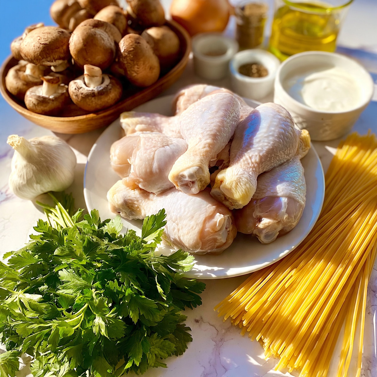 square image The image shows a white plate filled with raw chicken drumsticks placed on a white marbled surface. Surrounding the plate are various ingredients: a bunch of fresh green parsley at the front, a bundle of uncooked spaghetti pasta arranged diagonally, a wooden bowl filled with whole brown mushrooms, a small white bowl containing a white creamy sauce, a glass cup with golden olive oil, a bulb of garlic, an onion, and two small containers of spices. The scene is bright and organized, with natural lighting highlighting the fresh textures of the ingredients. photo taken with an iphone --ar 4:5 --v 7