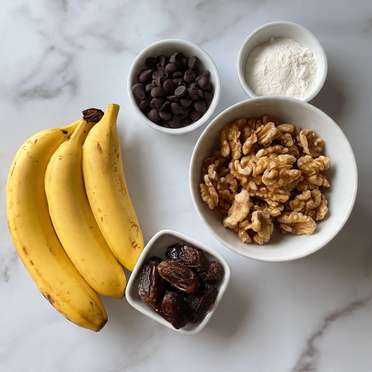 square image The image shows five ingredients on a white marbled surface, each placed in small white bowls or dishes. On the left, three yellow bananas with brown spots rest beside a small white dish filled with dark brown dried dates at the bottom. Above the dates, another small white dish contains dark round chocolate chips. On the right side, a medium white bowl is filled with light brown walnuts, showing their rough textured surfaces. Next to the walnuts, a small white dish holds a fine white powder, likely flour. Photo taken with an iphone --ar 4:5 --v 7
