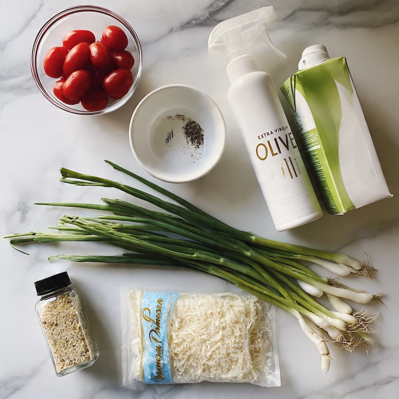 square image The image shows ingredients neatly arranged on a white marbled surface, including a small clear bowl of red grape tomatoes positioned top left, a white bowl with salt and pepper marked inside it below the tomatoes, and a white bottle of extra virgin olive oil spray placed next to a green and white carton of liquid egg whites on the right side. Near the bottom, fresh green onions with white bulbs and roots are laid horizontally, above a clear package of grated Parmesan cheese with blue and gold label text. In the bottom left corner, there is a clear bottle of garlic granules with a black cap. photo taken with an iphone --ar 4:5 --v 7