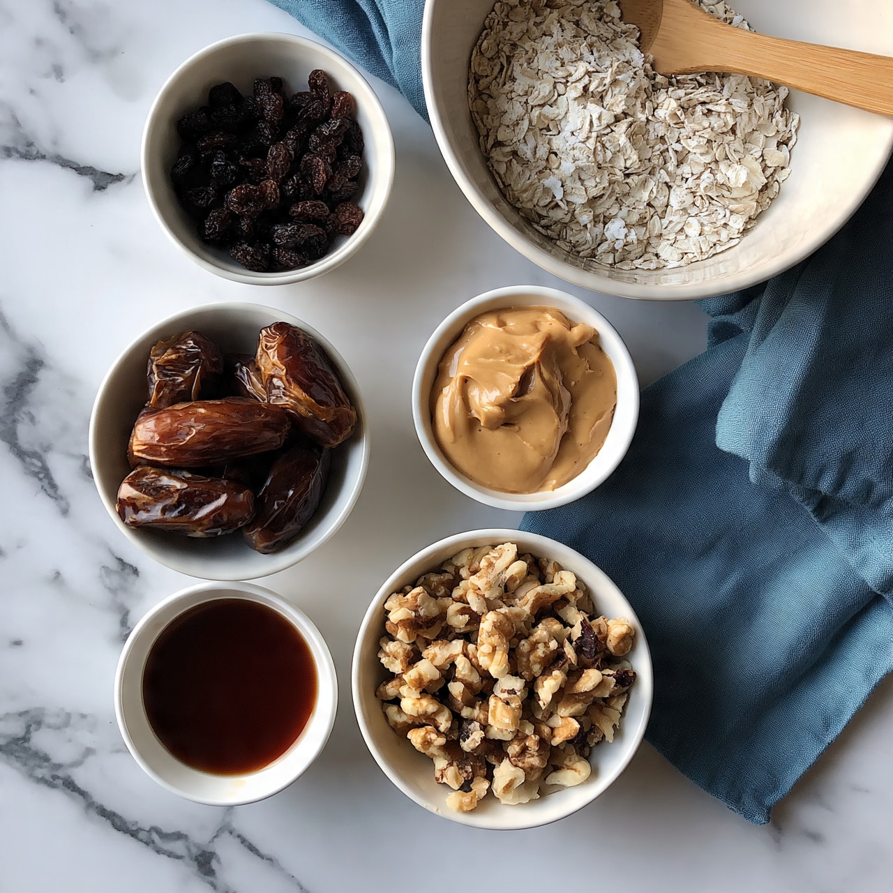 square image The image shows six white bowls on a white marbled surface, each with different food items. Starting from the top right, there is a large white bowl filled with white oats, with a wooden spoon resting inside it. To the top left sits a smaller bowl filled with dark raisins. Below the oats, a small bowl contains light brown peanut butter with a smooth texture. Directly below the raisins, there is a bowl filled with dark brown dates. To the right of the dates, a small bowl has dark brown liquid, likely vanilla or syrup. At the bottom center, a bowl holds chopped walnuts with varying shades of light and dark brown. A blue cloth is placed beneath some of the bowls on the marbled surface. Photo taken with an iphone --ar 4:5 --v 7