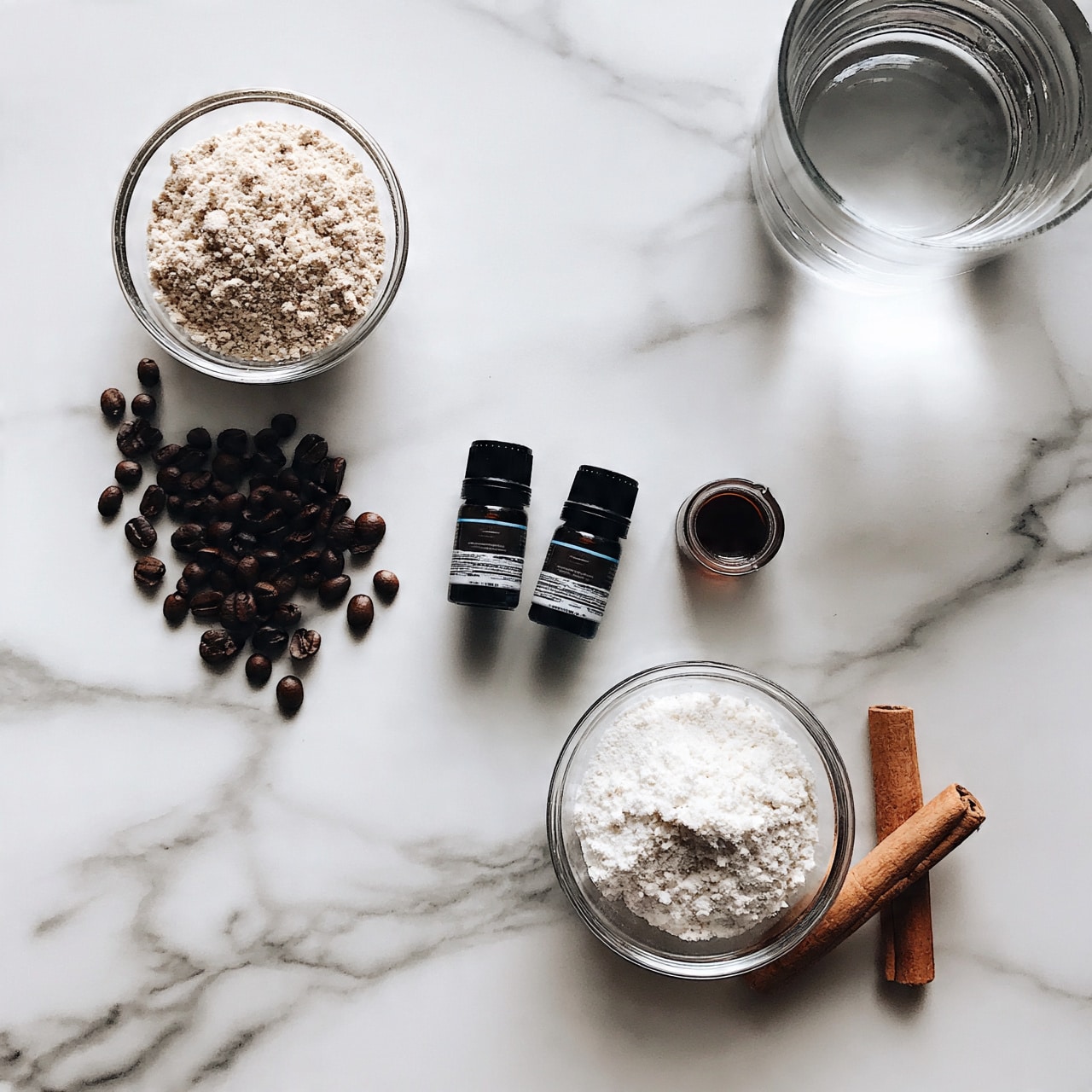 square image The image shows a white marbled surface with several items placed on it. In the top left, there is a small clear glass bowl filled with light beige powder. Below it, scattered on the surface, are dark brown coffee beans. Near the center, there are two small dark bottles with labels, and to their right, a tiny glass container with dark brown liquid. Below these, a small clear bowl holds a white, powdery substance. At the bottom right, two cinnamon sticks rest beside the bowl. Near the top right corner, a clear glass of water is placed. The composition is neat and well spaced. Photo taken with an iphone --ar 4:5 --v 7square image