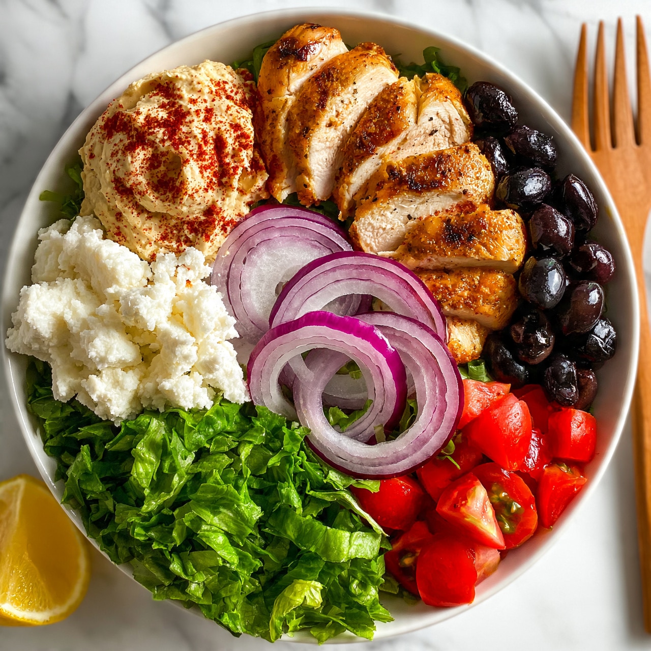 square image A white bowl on a white marbled surface holds a colorful, fresh salad arranged in layers and sections. On the top right side, there are slices of golden-brown cooked chicken arranged neatly. Next to the chicken, black olives add a dark, glossy contrast. Moving left, there is a scoop of creamy hummus sprinkled with red spices. Below the hummus, white crumbled cheese is softly piled. In the middle, several crisp rings of purple-red onion rest on a bed of bright green chopped lettuce, which fills the bottom left of the bowl. Cherry tomatoes cut into small pieces sit next to the cheese on the bottom right. A wedge of yellow lemon is placed on the far left side near the lettuce. A wooden fork is on the right edge, resting partly inside the bowl. Photo taken with an iphone --ar 4:5 --v 7