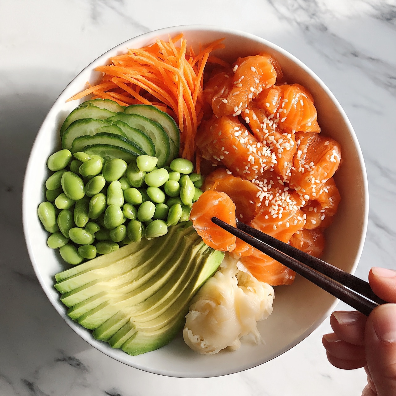 square image A white bowl filled with a colorful poke bowl is shown on a white marbled surface. The bowl has five main layers: bright orange pieces of marinated raw salmon sprinkled with white sesame seeds at the top right, fresh green sliced avocado fanned out on the bottom left, vibrant light green edamame beans next to the avocado, thinly sliced cucumber and shredded orange carrots layered at the top left, and a small pile of creamy white pickled ginger at the bottom center. A woman's hand is holding dark chopsticks picking up a piece of salmon from the bowl. The textures are fresh and juicy for the salmon, smooth and creamy for the avocado, and crisp for the vegetables. Photo taken with an iphone --ar 4:5 --v 7