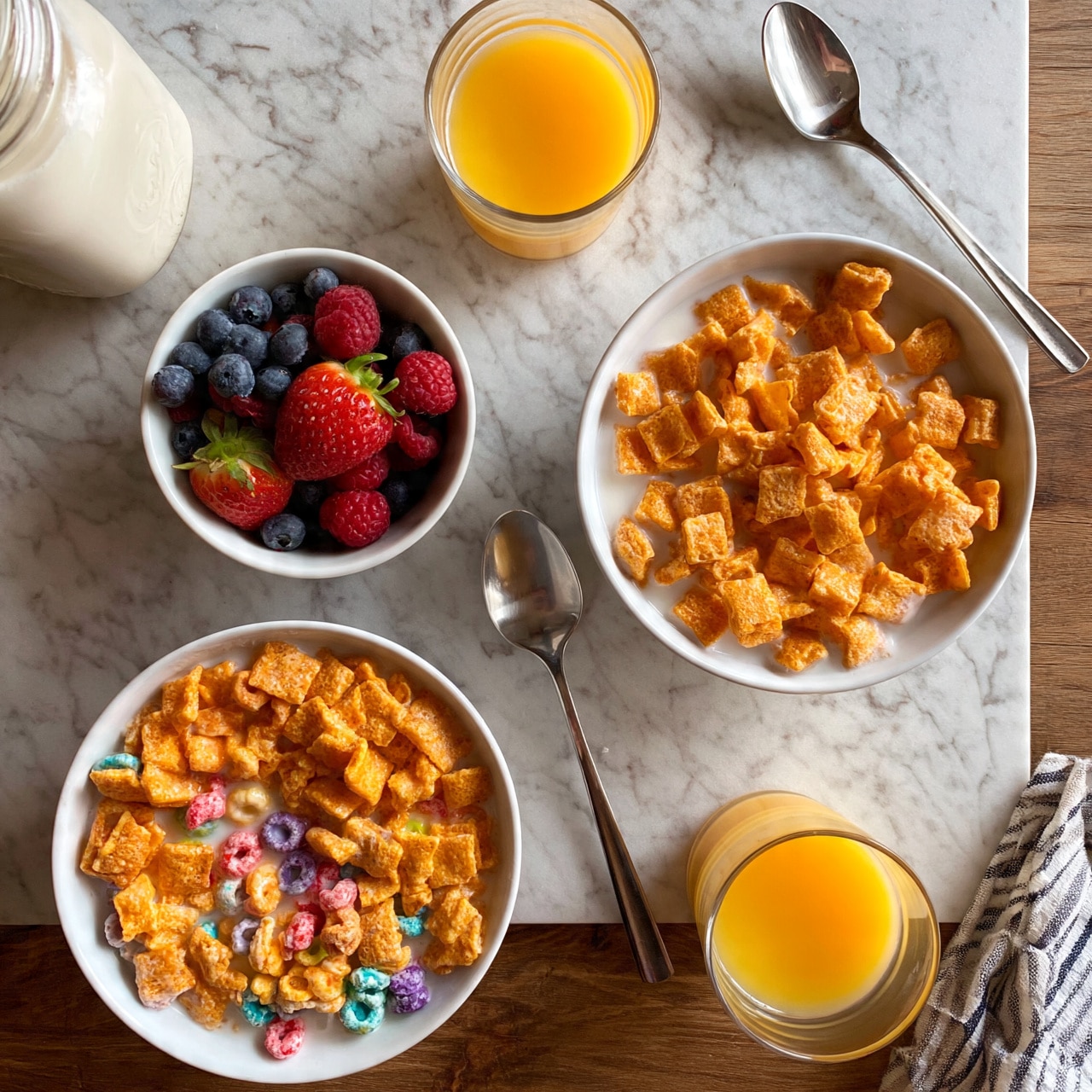 square image The image shows a breakfast scene on a white marbled texture with a wooden table underneath. There are two main white bowls of cereal filled with milk: one on the right filled with orange square cereal pieces, and one on the bottom left filled with orange square cereal pieces with colorful round cereal pieces mixed in. To the left of the bowl on the right, there is a small white bowl full of fresh berries including strawberries, blueberries, and raspberries. There are two glasses of orange juice, one towards the top center and one near the bottom right. Two metal spoons are placed on the table, one next to each bowl. A jar of milk is on the far left, partially out of the frame. A striped cloth napkin is visible on the bottom right corner. The photo taken with an iphone --ar 4:5 --v 7