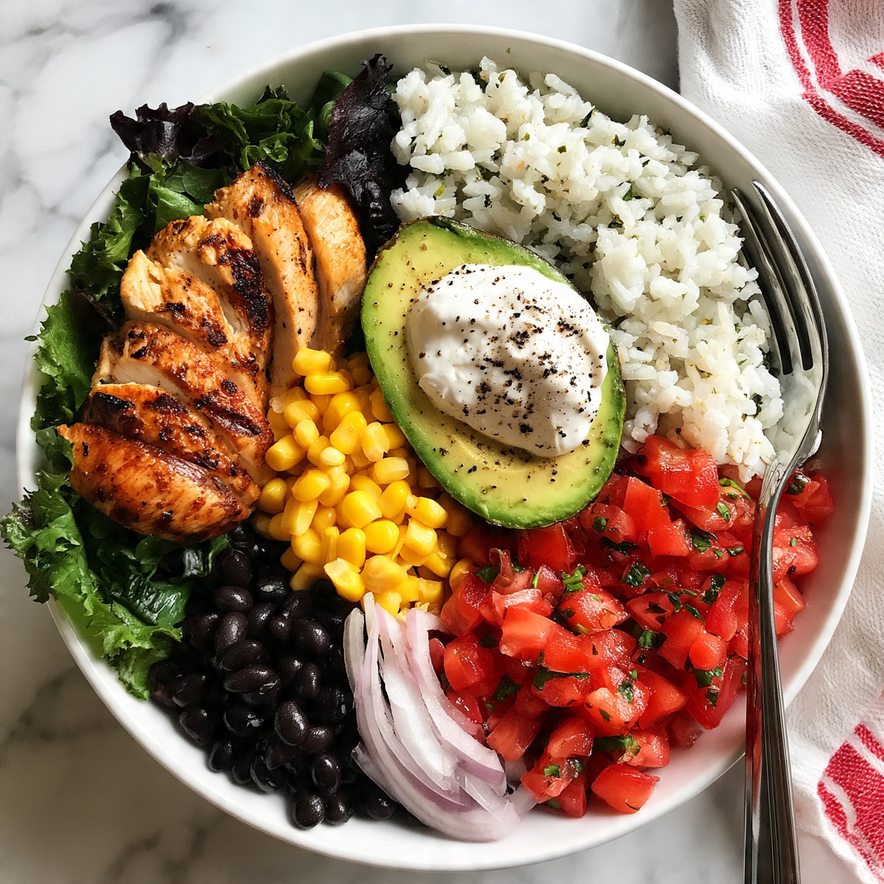 square image A white bowl filled with multiple colorful layers arranged neatly in sections. Starting from the left, grilled chicken slices with a slightly charred brown color rest on a bed of dark green leafy lettuce. Next to it, bright yellow corn kernels form a small mound. On the bottom left, black beans sit near thin slices of light purple onion. To the right, vibrant red diced tomatoes scattered with small green herbs create a fresh look. White rice mixed with tiny bits of herbs fills the top right side. At the center rests a halved avocado topped with a dollop of white sour cream sprinkled with black pepper. A silver fork rests against the rice side inside the bowl. The bowl is placed on a white marbled surface with a white cloth having red stripes beside it. Photo taken with an iphone --ar 4:5 --v 7