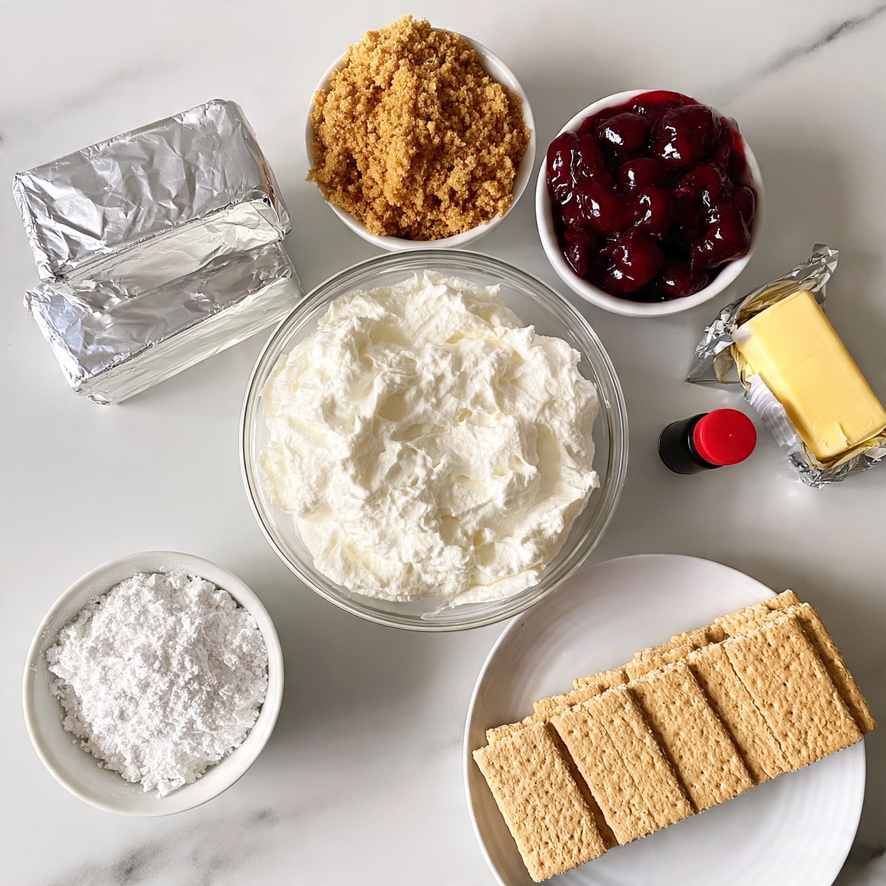 square image The image shows a flat lay of various dessert ingredients arranged on a white marbled surface. There is a clear glass bowl in the center filled with smooth, white whipped cream-like texture. Above the bowl, there are two small white bowls, one filled with crumbly brown sugar and the other with a glossy, deep red cherry topping. To the left, two wrapped silver blocks of cream cheese are stacked. Below the cream cheese, a white bowl holds a fine, white powdered substance. At the bottom right, a white plate neatly holds a row of rectangular beige graham crackers. On the right side of the bowls, a small black bottle with a red cap is placed next to a wrapped stick of yellow butter. Photo taken with an iphone --ar 4:5 --v 7
