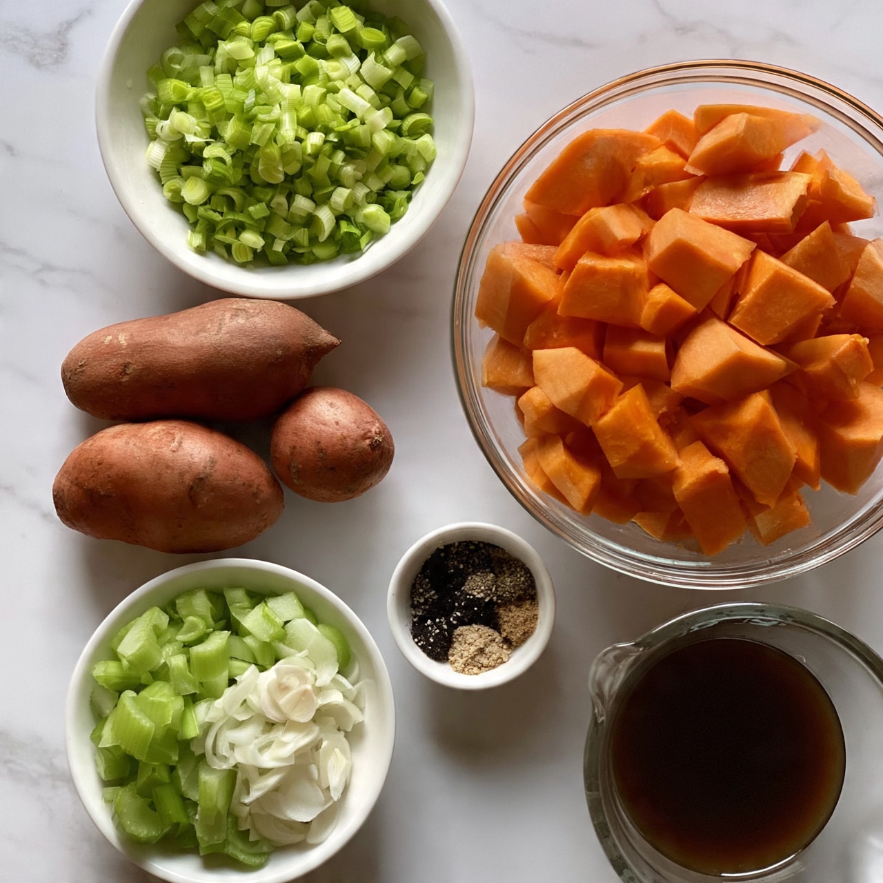 square image The image shows a top view of raw carved orange pumpkin pieces in a clear glass bowl on the right side. To the top left of the pumpkin bowl, there is a white bowl filled with finely chopped green leeks with a light green and white pattern. Below the leeks, three whole raw sweet potatoes with a reddish-brown skin are placed on the white marbled surface. Near the bottom left corner, there are two white bowls with chopped green celery and thinly sliced white garlic. In between, a tiny white bowl holds mixed black and light brown spices. On the lower right side, a clear glass measuring cup filled with dark brown liquid sits on the white marbled surface. The photo taken with an iphone --ar 4:5 --v 7