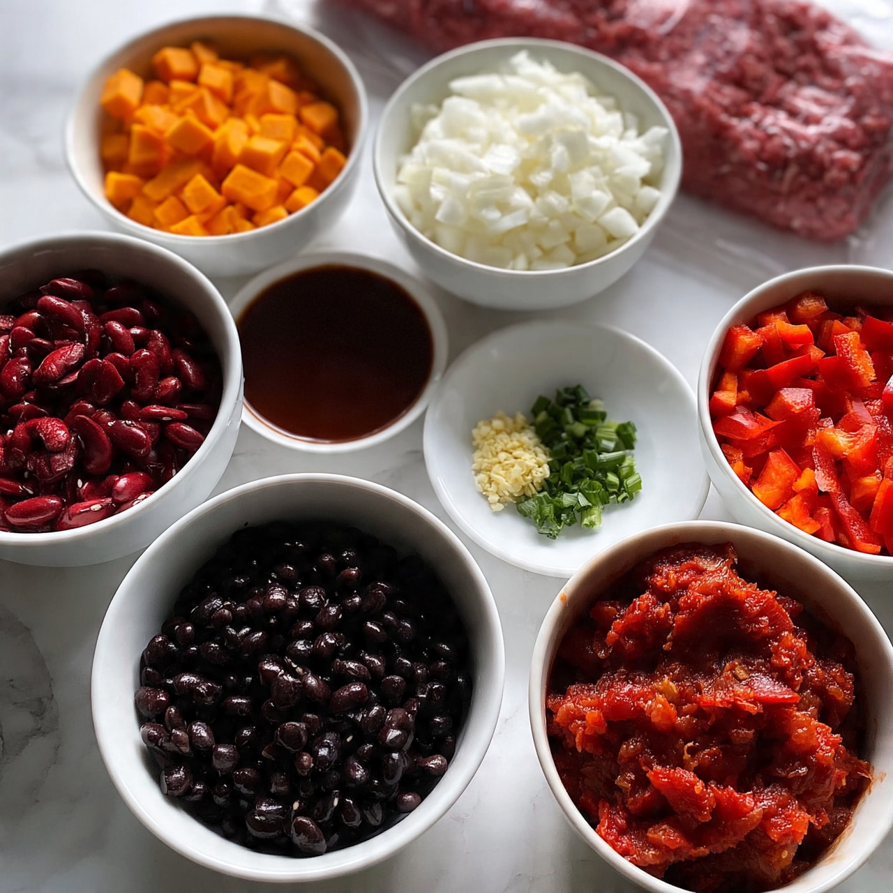 square image The image shows several white bowls and a white plate on a white marbled surface, each containing different ingredients. One bowl has small orange cubes of sweet potato, another contains chopped white onions, and a third is filled with chopped red bell peppers. There are also bowls with red kidney beans, whole black beans, a dark brown liquid, crushed tomatoes, and tomato paste. A small white plate holds minced garlic and chopped green onions. Next to the bowls, there is a package of raw ground beef visible. The arrangement is neat, and the ingredients are fresh and colorful, ready for cooking. Photo taken with an iphone --ar 4:5 --v 7