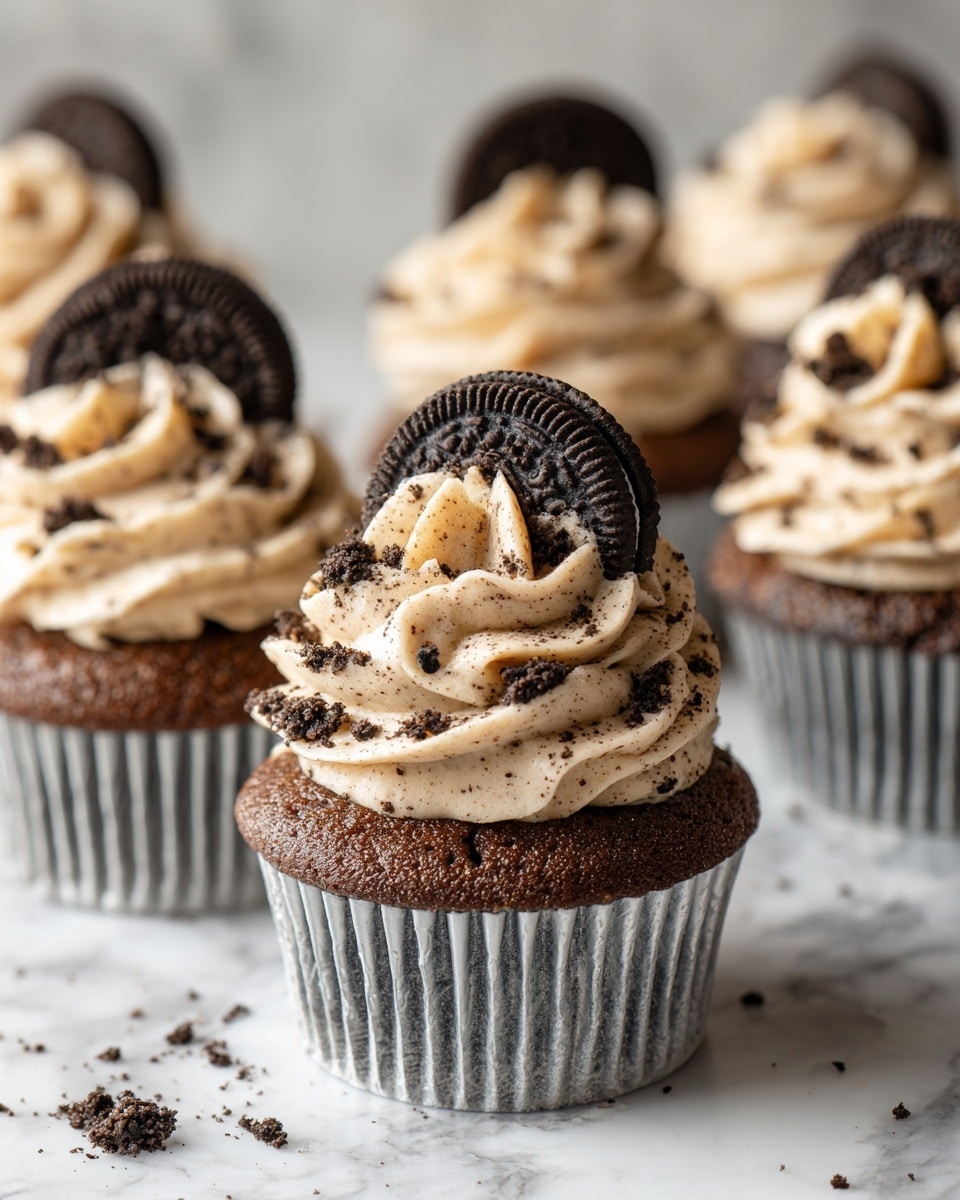 The image shows several chocolate cupcakes placed on a white marbled surface. Each cupcake has a dark brown base with a silver wrapper and is topped with a thick swirl of creamy, light beige frosting mixed with small dark cookie crumbs. On top of each frosting swirl, there is a whole Oreo cookie standing vertically. Some small cookie crumbs are scattered around the cupcakes on the surface, adding texture to the scene. The focus is sharp on the cupcake in the front, slightly blurring the others in the background. Photo taken with an iphone --ar 4:5 --v 7