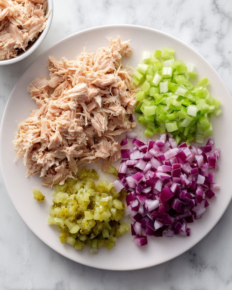 A white plate is placed on a white marbled surface, holding four separate piles: shredded light brown tuna on the left side, finely chopped light green celery at the top, diced purple-red onions on the right, and small pieces of green pickles at the bottom. To the upper left of the plate, a white bowl filled with more shredded tuna is partially visible. The scene is clean and bright, focusing on the fresh, raw ingredients. photo taken with an iphone --ar 4:5 --v 7