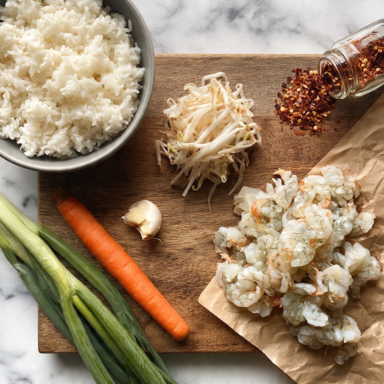 square image The image shows a wooden board with several cooking ingredients arranged neatly. On the top left, there is a gray bowl filled with white cooked rice. To the right of the bowl, there is a small pile of fresh bean sprouts. At the top right corner, there is a small glass container spilling red chili flakes. On the bottom right, raw peeled shrimp are spread partially on a brown paper. On the bottom left, there is a single carrot next to three long green onions, and a whole peeled garlic clove sits just above the carrot. The background is a white marbled surface. photo taken with an iphone --ar 4:5 --v 7