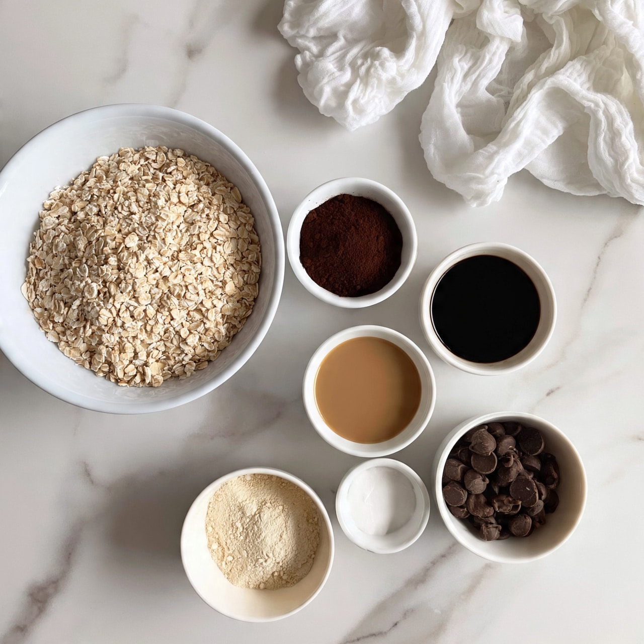 square image A top-down view shows seven white bowls arranged on a white marbled surface. The largest bowl at the top left is filled with light beige rolled oats. Around it, smaller bowls hold different ingredients: a dark brown powder on the top center, a black liquid next to it on the right, a light brown liquid below the black liquid, a white solid below that, dark brown chocolate chips to the right bottom, and a pale beige powder at the bottom left. A crumpled white cloth is placed near the top right corner. The image looks bright and clean with simple colors and textures. photo taken with an iphone --ar 4:5 --v 7