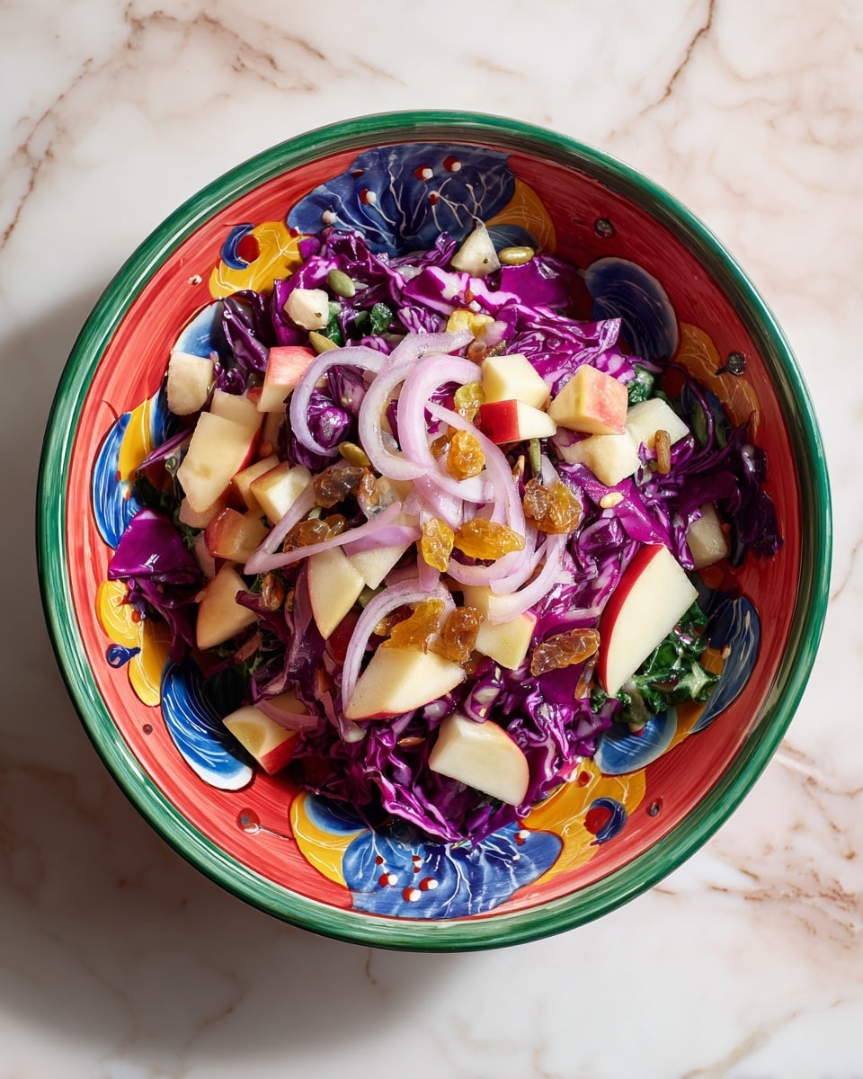 The dish shows a colorful salad in a decorative bowl with a green rim and red interior with painted blue drops and yellow swirls. The bottom layer is chopped purple cabbage with crisp, textured leaves. On top of that, there are small pieces of white and red apple chunks scattered around. Golden raisins are spread over the salad, adding a wrinkled texture. Thin, curved slices of light purple onion are spread unevenly on the top. The bowl sits on a surface with a white marbled texture. Photo taken with an iphone --ar 4:5 --v 7