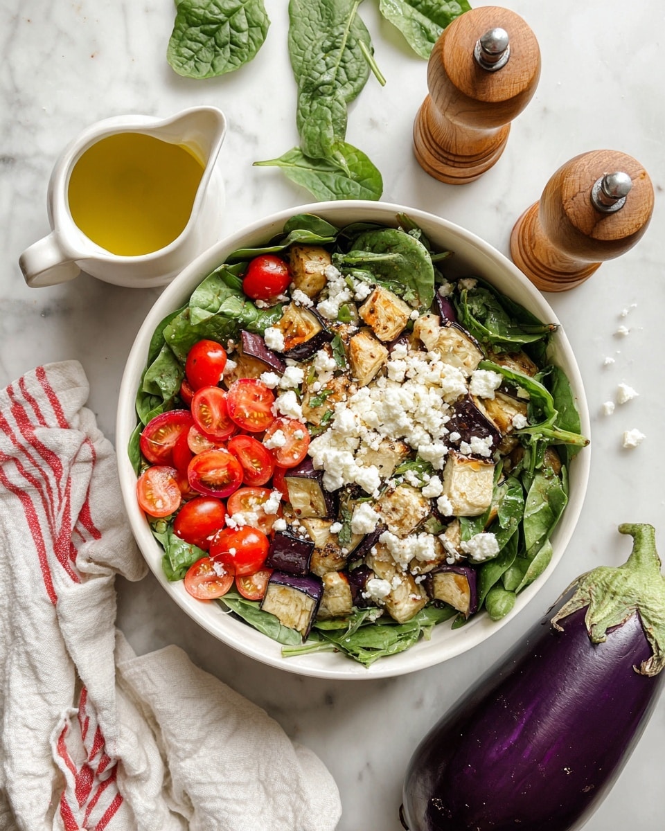 A white round bowl filled with a fresh salad showing three main layers: the base layer is a mix of dark green spinach leaves, the middle layer has bright red halved cherry tomatoes scattered evenly, and the top layer features small chunks of cooked purple eggplant with a light golden crust and white crumbled cheese sprinkled over everything. The bowl rests on a white marbled surface, with a small white sauce jug of yellow olive oil nearby, two wooden pepper and salt grinders positioned above, a whole raw purple eggplant to the right, and a white cloth with red stripes in the bottom left corner. photo taken with an iphone --ar 4:5 --v 7