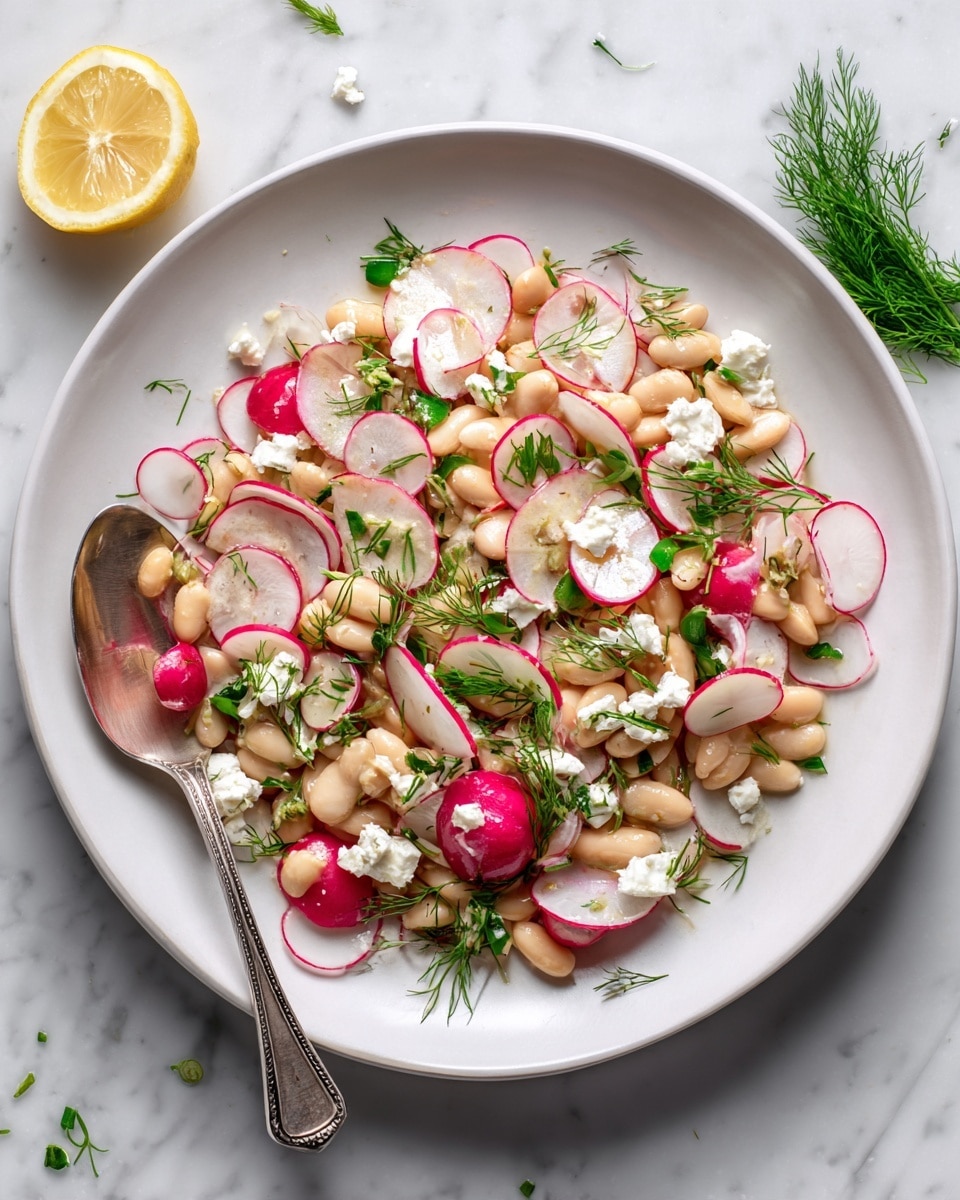 A white round plate filled with a salad made of white beans and thin round slices of radish with red edges scattered throughout. Small white crumb pieces of cheese are spread over the salad, along with bits of fresh green herbs layered on top. The salad has a light and fresh look with soft beige, white, red, and green colors mixed. A silver spoon rests on the left edge of the plate. The plate sits on a white marbled surface with a lemon wedge and some dill nearby. photo taken with an iphone --ar 4:5 --v 7