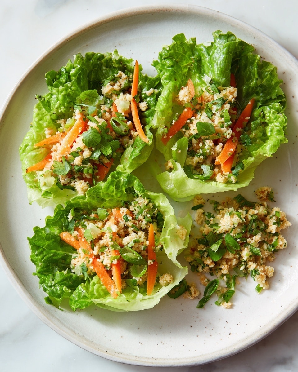 The dish shows three layers on a white plate with a white marbled background. The first layer is bright green curly lettuce leaves acting as cups, each leaf textured and fresh-looking. The second layer consists of thin, soft orange carrot strips placed both inside the lettuce and spread on the plate. The top layer is light beige small crumbled pieces mixed with some green herbs, evenly spread on each lettuce leaf and a bigger pile to the right on the plate. The whole dish looks fresh with a mix of soft, crunchy, and slightly coarse textures, arranged neatly in a circular form. Photo taken with an iphone --ar 4:5 --v 7