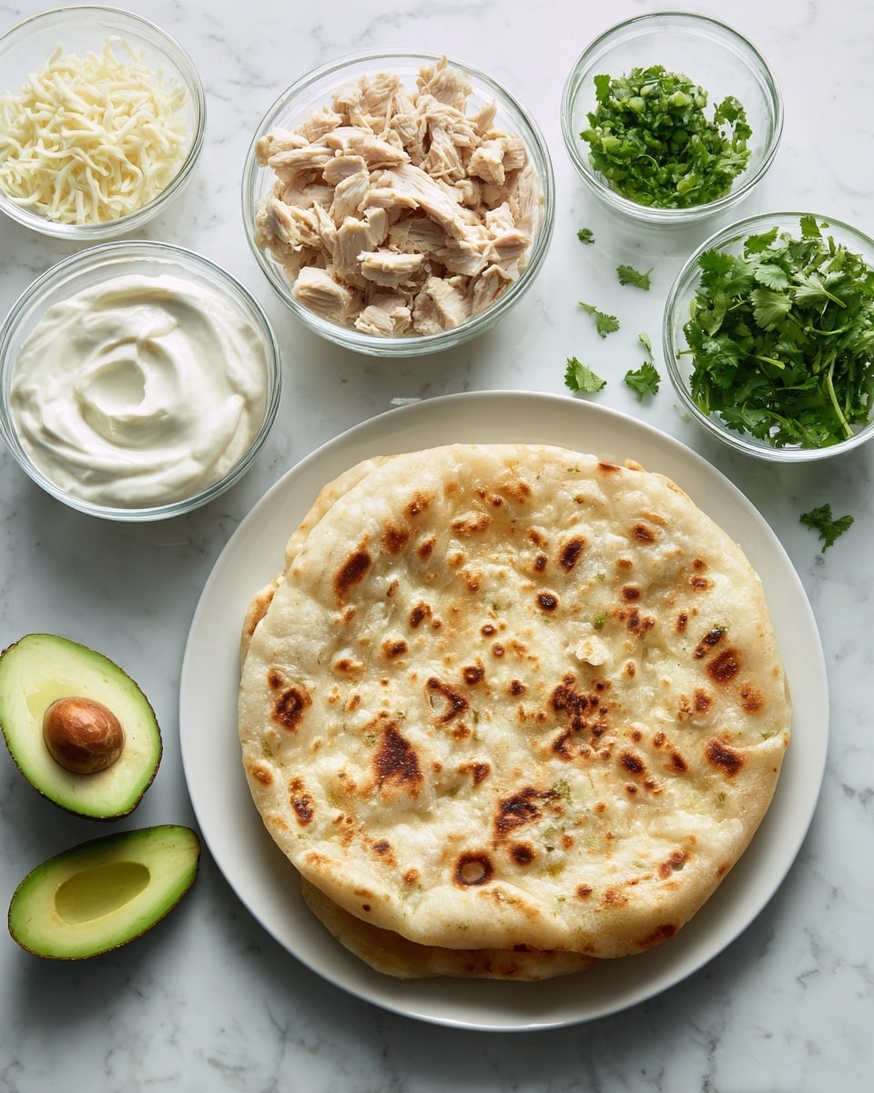 The image shows a white plate with a round flatbread that is light brown with small darker spots and a few small holes on its surface in the center. Around the plate are five clear glass bowls: one with shredded white cheese, another with chopped cooked chicken pieces that are beige and white, one with a creamy white sauce that has a swirled texture, one smaller bowl with fresh green cilantro leaves, and two halves of a green avocado with a smooth green inside and a darker green skin placed next to each other. The items sit on a white marbled surface. photo taken with an iphone --ar 4:5 --v 7