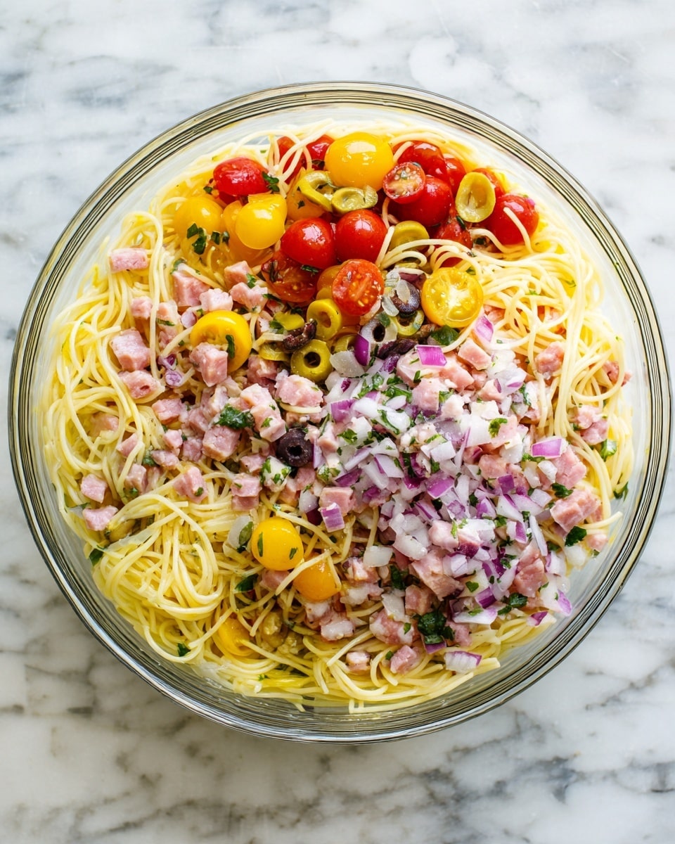 A clear glass bowl filled with a pasta salad that has three main layers: the first layer is thin, yellow noodles that are soft and mixed throughout; the second layer includes colorful chunks of red and yellow cherry tomatoes, small rings of light yellow pepper, sliced black olives, and small pieces of green herbs; the third layer has small cubes of pinkish sausage and finely chopped red onion, all evenly spread on top and mixed in. The bowl is placed on a white marbled surface. photo taken with an iphone --ar 4:5 --v 7