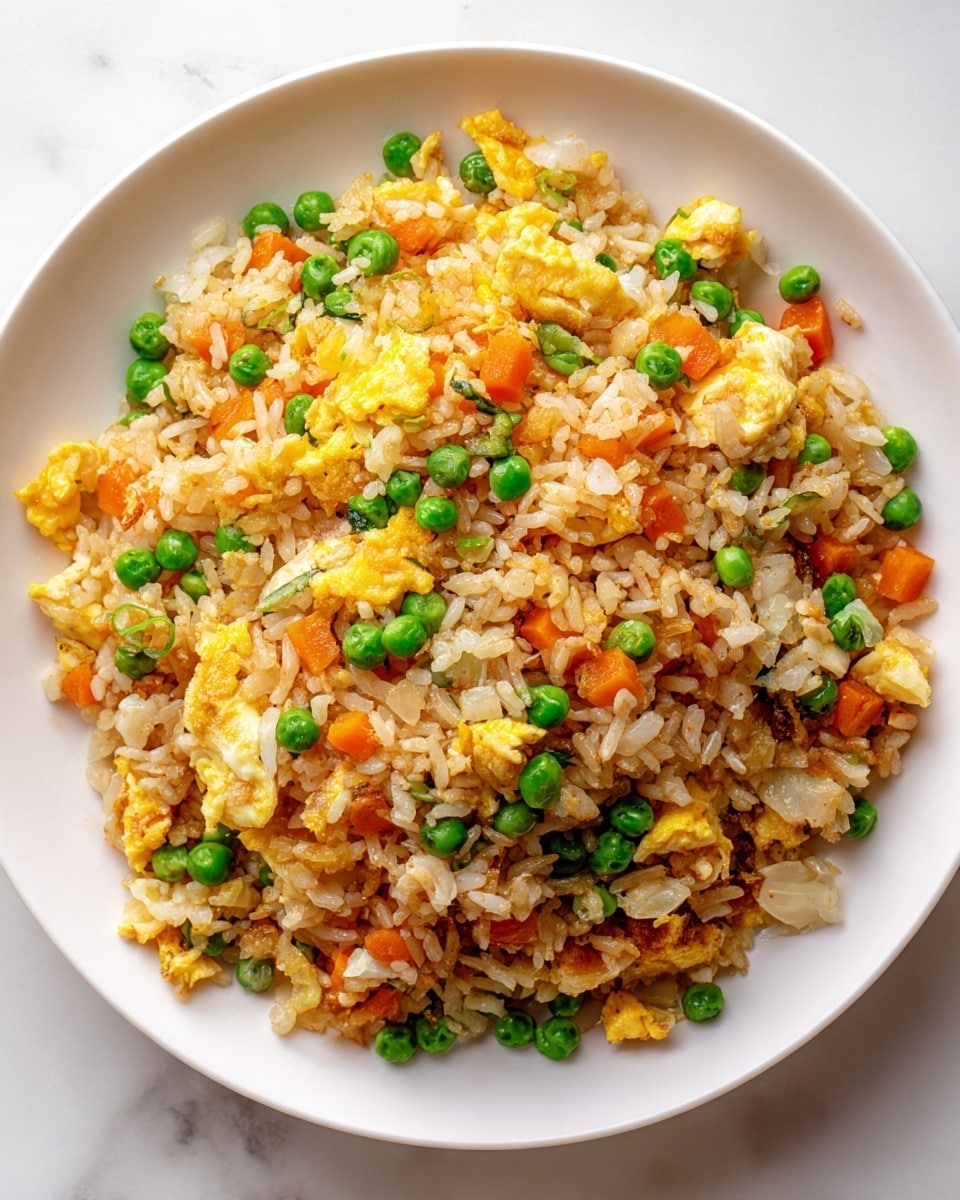A white plate filled with a colorful fried rice dish with distinct layers showing light brown cooked rice, bright green peas scattered evenly, small orange carrot cubes, and soft yellow scrambled egg pieces mixed throughout. The texture of the rice looks slightly sticky but fluffy, with tiny bits of translucent diced onions visible among the rice and vegetables. The dish sits on a white marbled surface, giving a clean and fresh background. photo taken with an iphone --ar 4:5 --v 7