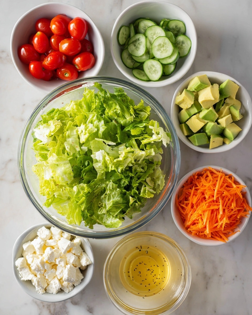 A clear glass bowl sits in the middle filled with bright green leafy lettuce arranged loosely. Surrounding it are five small white bowls: one with halved red cherry tomatoes at the top left, a second with thin green cucumber slices at the top right, a third at the bottom right filled with chunks of light green avocado, a fourth at the bottom left containing white crumbled cheese, and the last one near the bottom center holding shredded orange carrots. To the right of the main bowl is a small clear glass container of light yellow salad dressing with visible black specks. All items rest on a white marble surface. Photo taken with an iphone --ar 4:5 --v 7