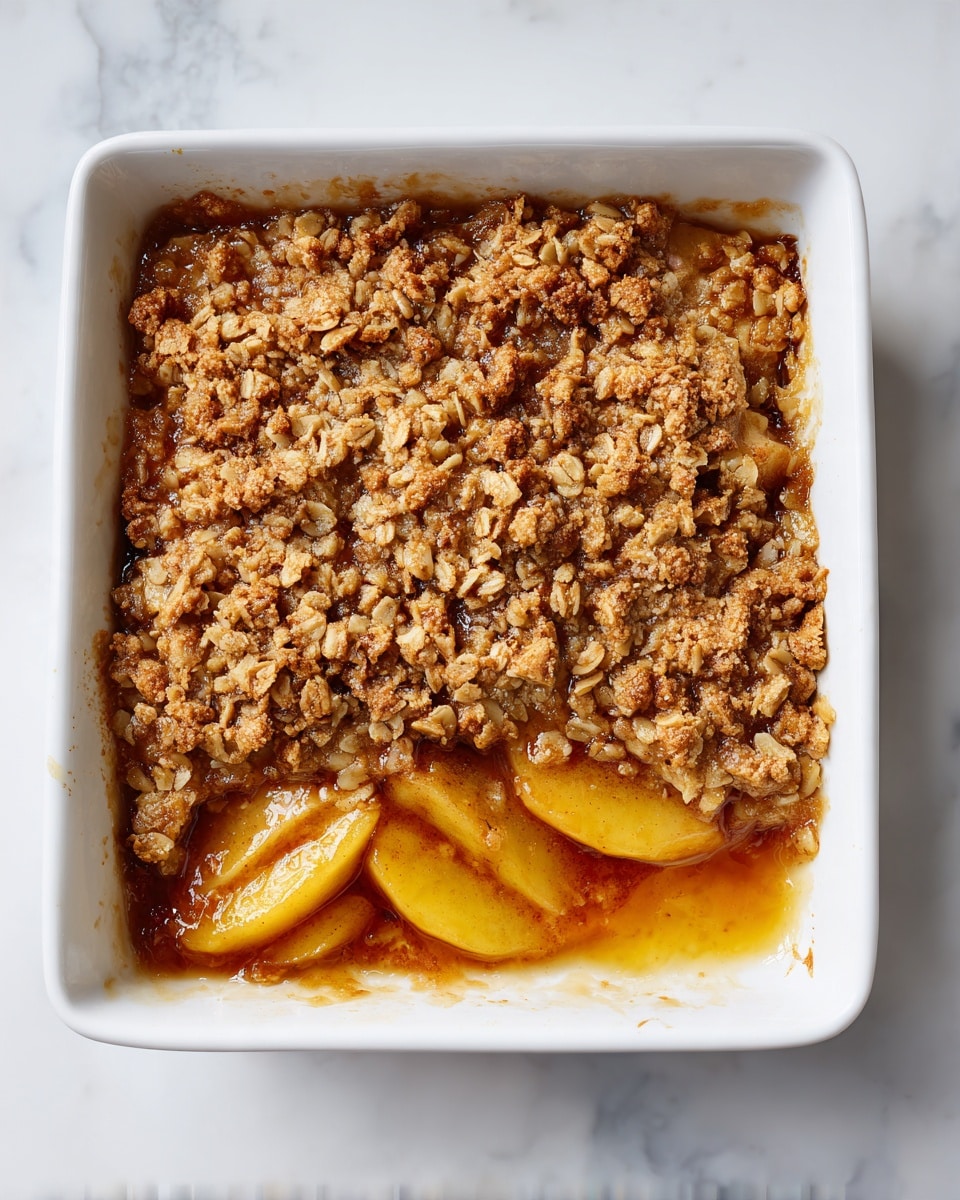 A baked dessert in a white square ceramic dish with three layers visible: the bottom layer shows thin reddish-brown fruit slices, likely apples, soft and cooked; the middle layer is a thick, syrupy, caramel-colored sauce soaking the fruit; the top layer is a golden-brown crumbly mixture made of oats and brown sugar, textured and uneven with small clusters all over. The dish is on a white marbled surface. photo taken with an iphone --ar 4:5 --v 7